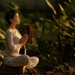 Serene scene of a woman meditating in a lush garden setting at daylight.
